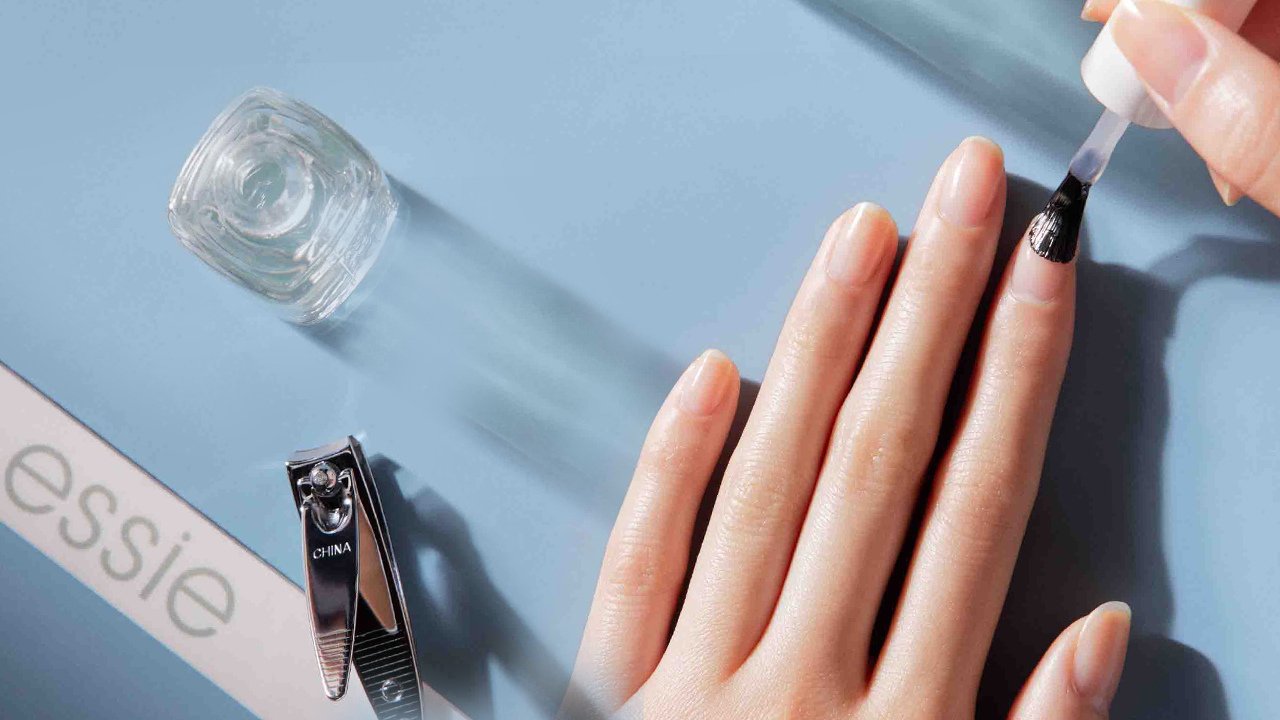 a woman applying essie hard to resist advanced clear nail strengtheners onto her nail